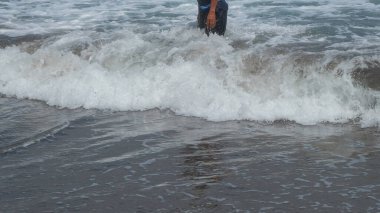 Bir adamın ayağı büyük bir dalga tarafından vuruldu. Deniz dalgaları tarafından vurulan bir insanın tasviri