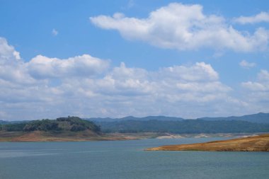 Gündüz vakti mavi gökyüzü ve beyaz bulutlarla gölün manzarası. Gölün kenarındaki karanın şekli ve şekli. Dinlenme yeri.