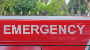 Ambulansta beyaz büyük harflerle EMEGENCY yazıyor. Kırmızı arkaplan. Acil durumlar için ambulans