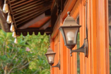 Duvara asılmış eski bir lamba. Lambanın şekli eski görünüyor. Demirden ve şeffaf camdan yapılmış. Bahçeler ve açık hava ışıkları için ışıklar