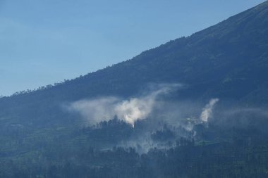 Bir dağ yamacında yanan tarımsal arazinin dumanı. Dağın yamaçlarında beyaz duman. Çiftçiler ekin kalıntılarını temizliyor