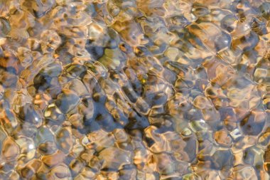 Net nehir suyunun soyut şekilleri, desenleri ve dokuları doğal kayalarla dalgalanır. Yukarıdan görünen küçük nehir kayaları. Çevresel konsept. Doğal su, kaya deseni ve doku arka planı. Grafik tasarımı veya afiş arkaplanı için