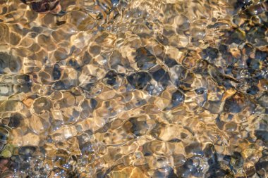Net nehir suyunun soyut şekilleri, desenleri ve dokuları doğal kayalarla dalgalanır. Yukarıdan görünen küçük nehir kayaları. Çevresel konsept. Doğal su, kaya deseni ve doku arka planı. Grafik tasarımı veya afiş arkaplanı için