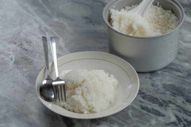 Yemek masasında bir tabak beyaz pirinç. Tabaklar, kaşıklar, çatallar ve pilav tencereleri. Karbonhidrat kaynakları kavramı. Uzayı metin için kopyala. Grafik tasarımı için