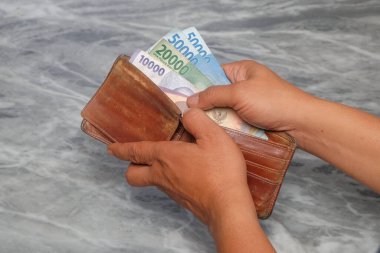 Kahverengi deri cüzdandan banknotlar alınıyor. Finansal ve iş konseptleri. Endonezya rupia banknotları. Grafik tasarımı veya finansal haber makaleleri için.