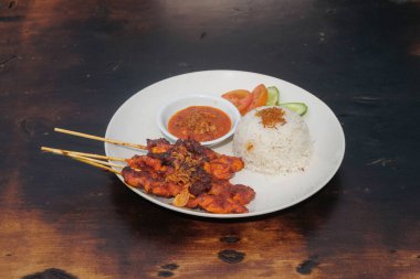 Masanın üzerine bir tabak sığır eti ve pilav koy. Acı biber sosu ve dilimlenmiş salatalık karışımı ile sığır eti satay. Tipik Endonezya yemekleri. Grafik tasarımı için, 3B görüntüleme ve pankart arkaplanı