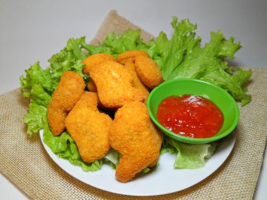 Lezzetli tavuk nugget ve domates sosu marul ya da su teresi ile servis edilmiş, beyaz arka planda izole edilmiş..