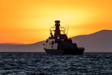 NATO savaş gemisi İzmir körfezinde turuncu gün batımı ışığında