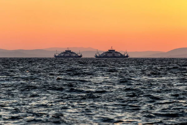 在夕阳西下的天空和远山的背景下 有两艘渡船在波涛汹涌的大海中相互驶向对方 — 图库照片
