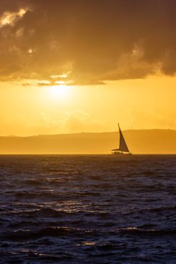 Fırtınalı denizde, turuncu gün batımında yelkenli.