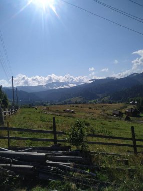 Dağları ve Açık Mavi Gökyüzü olan huzurlu kırsal alan. Yüksek kaliteli fotograf. Yeşil tarlalar, ahşap çitler ve parlak güneşli gökyüzünün altındaki uzak dağlardan oluşan sakin bir kırsal manzara. Mükemmel.