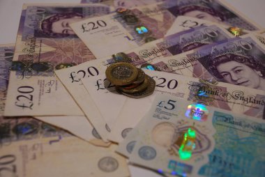 Zenginlik ve finansı sembolize eden küçük bir para yığınının yanında çeşitli mezheplerin yer aldığı bir İngiliz banknotları koleksiyonu. Canlı para birimi ayrıntıları ekonomik kavramları yansıtıyor.