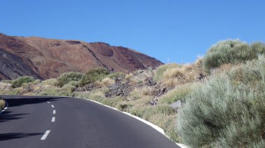 Kıvrımlı yol, berrak mavi gökyüzünün altındaki engebeli bir dağ ve çöl arazisinde esiyor. Seyahat, keşif, yol gezileri ve macera temaları için ideal.