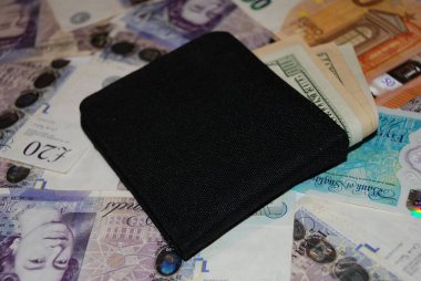 A black wallet sits atop various international currency notes, including us dollars, euros, and pounds, symbolizing global finance and economic diversity. clipart