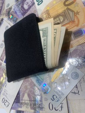 A black wallet filled with us dollar bills rests on banknotes of euros and pounds, showcasing a mix of international currencies and financial diversity. clipart