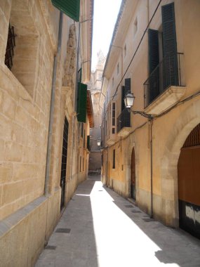 Eski taş binalar arasında uzanan sessiz dar bir ara sokak gün ışığını karşılıyor. Güneş uzun gölgeler bırakır, bu tarihi şehir merkezinin cazibesini arttırır..