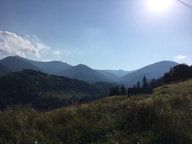 Bereketli yeşil vadiler ve görkemli dağlar berrak mavi gökyüzünün altına kadar uzanıyor. Güneş ışığı araziye gölge düşürür, sakin bir doğal manzara yaratır..