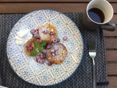 Üzerinde pudra şekeri ve taze böğürtlenlerle birlikte bir fincan kahveyle birlikte tatlı krepler bulunan enfes bir kahvaltı seti. Yemek zarif bir tabakta servis edilir..