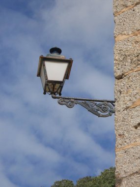 Klasik bir sokak lambası, mavi gökyüzü ile güzel zıt, taş bir bina üzerine monte edilir. Lambanın karmaşık tasarımı iyi korunmuş mimariye cazibe katıyor..