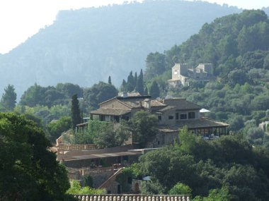 Dağlık bir arazide yemyeşil yemyeşil bir villa arasında yuva yapmış. Yapı geleneksel mimariye sahiptir ve açık mavi bir gökyüzünün altındaki ağaçlarla çevrilidir..