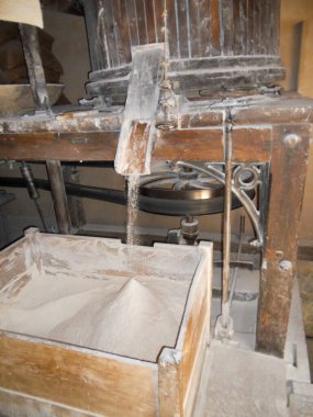 Antika makineler tahılları un haline getirme sürecini sergiliyor. Toz bulutları yükselir, kırsal bir ortamda bu zamanın şerefli ekipmanlarının işçiliğini ve işlevselliğini vurgular..