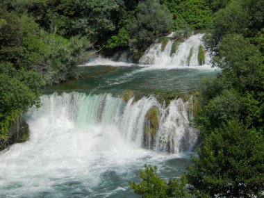 Su birçok kaya katmanının üzerinden zarifçe akar ve çarpıcı bir şelale oluşturur. Yemyeşil yeşillikler manzarayı çerçeveler, doğanın güzelliğini vurgular ve sükuneti davet eder.