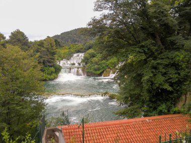 Çarpıcı bir şelale canlı yeşil ağaçların arasından yavaşça akar ve sakin bir manzara yaratır. Suyun huzurlu sesi, doğanın sakin atmosferini tamamlar..