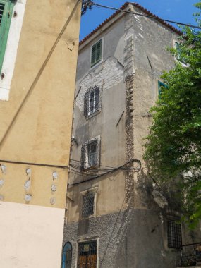 Dar sokakların kesiştiği yerde, eski bir bina var. Duvarları soyulmuş ve yıpranmış. Güneş ışığı dokuyu aydınlatır, tarihi bir mahallenin özünü yakalar..