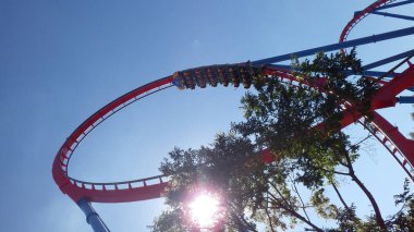 Sürücüler, açık mavi bir gökyüzüne karşı döngü içinde süzülürken heyecan verici bir lunapark trenine binerler. Güneş ışığı ağaçların arasından süzülür ve canlı atmosfere katılır..