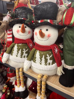 Two cheerful snowmen dressed in festive outfits sit happily among holiday decorations. Their green and red apparel features winter themes, making them ideal for seasonal festivities. clipart