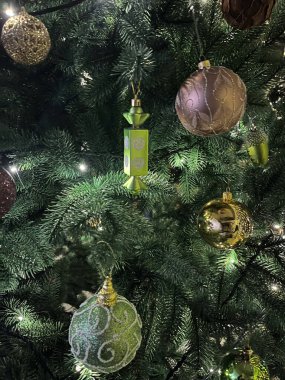 Yeşil, altın ve mor renklerde çeşitli süslerle süslenmiş canlı bir Noel ağacı..