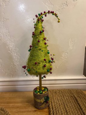 Renkli süslemeleri olan parlak yeşil bir ağaç ahşap bir yüzeyde oturur. Bu büyüleyici parça ev ortamını güzelleştiriyor. Tatil kutlamaları için mükemmel..
