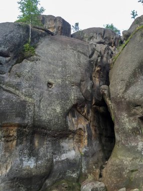 Görkemli kaya oluşumları, bulutlu bir gökyüzünün altında karmaşık dokuları ve desenleri olan uzun boylu dururlar. Yeşillik, bu eşsiz manzaranın doğal güzelliğini de ekliyor..