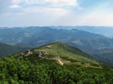 Yuvarlanan tepelerin ve dağların geniş manzarası yemyeşil ve kayalık arazilerin karışımını gösteriyor..