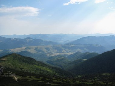 Açık mavi gökyüzünün altında nefes kesici manzaralar katmanlı tepeler ve vadiler. Güneş ışığı yumuşak gölgeler bırakır, uzaktaki sakin yabanın güzelliğini arttırır..