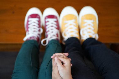 İki insan, bacakları açık şekilde yan yana oturur. Spor ayakkabılarının tabanına bulanık bir efektle dokunurlar. Her iki şahıs da ellerini ayakkabılarının birleştiği yerde tutarak sevgi ve pozitiflik mesajı veriyor..