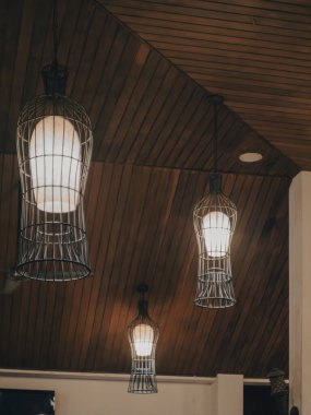 Kablo yapısı olan üç kolye lambası ahşap bir tavandan sarkıyor, boyutları en büyükten en küçüğe değişiyor, şık ve modern bir görünüm yaratıyor..