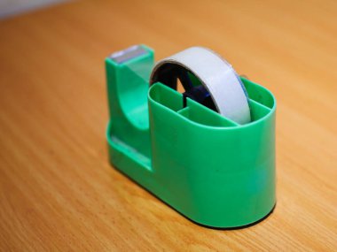 Ahşap bir yüzeyde yeşil bant dağıtıcısı, biraz bulanık, günlük ofis hayatı hissi yaratıyor..