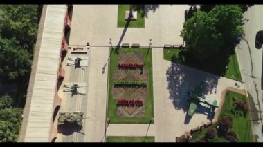 Ortasında büyük yeşil bir uçak olan bir park manzarası. Uçak çiçekler ve ağaçlarla çevrili.