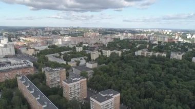 Büyük bir apartman kompleksi de dahil olmak üzere eski ve yeni binaların karışımına sahip şehir manzarası. Gökyüzü bulutlu ve ağaçlar yeşil