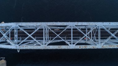 Köprü görüntüde, bir su kütlesi boyunca uzanan büyük beyaz metal bir yapı ile gösterilir. Köprü eski ve paslı görünüyor. Ürkütücü ve uğursuz bir görüntü veriyor.