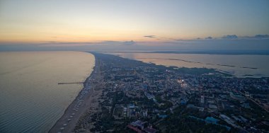 Şehir silueti uzaktan görülebilir, arkada okyanus var. Gökyüzü turuncu ve pembe renklerin güzel bir karışımıdır. Huzurlu ve huzurlu bir atmosfer yaratır.