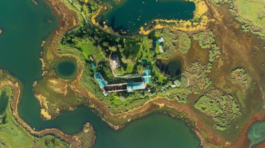 Ortasında küçük bir ada olan bir göl manzarası. Ev suyla çevrili ve etrafında birkaç küçük gölet var.