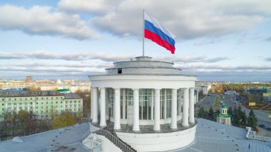 Üstünde bayrak olan büyük beyaz bir bina. Bayrak kırmızı, beyaz ve mavi.