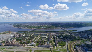 Şehir manzarası ve içinden bir nehir geçiyor. Gökyüzü çoğunlukla bulutlu ve birkaç beyaz bulut