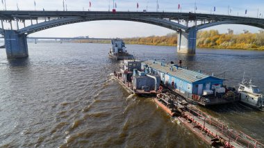 Büyük tekne daha küçük bir tekne tarafından çekiliyor. Sahne sakin ve huzurlu, su gökyüzünü yansıtıyor.