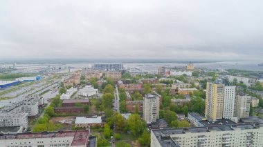 Şehir manzarası bulutlu bir gökyüzü ve arka planda bir nehir. Binalar yüksek ve bölgede birçok ağaç var.