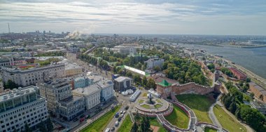 Ortasında büyük yeşil bir park olan şehir manzarası. Park binalar ve büyük bir su kütlesiyle çevrilidir. Gökyüzü açık ve güneş parlıyor. Nizhny Novgorod