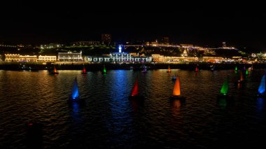 Bir grup renkli yelkenli gece bir gölde yüzüyor. Teknelerdeki ışıklar neşeli bir atmosfer yaratıyor. - Evet. Nizhny Novgorod