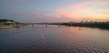 Arka planda köprü olan bir nehrin üzerinde güzel bir gün batımı. Gökyüzü bulutlarla dolu ve su sakin. Nizhny Novgorod